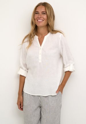 White linen blouse with a mandarin collar, three-button placket, and rolled sleeves, paired with light striped pants.