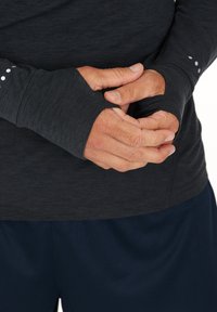 Langärmliges, schiefergraues Oberteil mit Daumenlöchern; weicher Stoff, schmale Passform und kleine weiße Punkte am Ärmelsaum. Dazu navyfarbene Shorts.