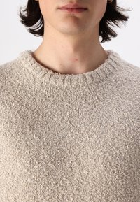 Beige textured knit sweater with a ribbed crew neckline. The fabric appears soft and slightly fleecy, with a subtle, uneven pattern.