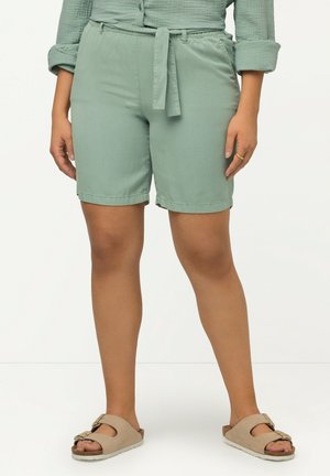 Grønne vævede stofshorts med bæltestrop, der har foldede manchetter. Kombinationen med beige slidesandaler.