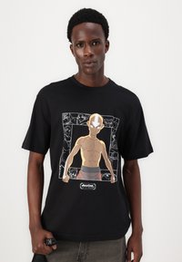 Sort bomuld T-shirt med et graphic af en karakter med en solbrun hudtone og en barberet hoved, omridset i hvidt mod en tegneserieinspireret baggrund.