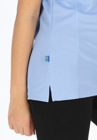 Lyseblå sports-top med tekstureret stof, sideslids og lille svensk flag accent på kanten, parret med sorte leggings.
