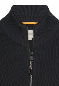 Granatowy sweter zapinany na suwak z prążkowaną fakturą i wysokim kołnierzem. Posiada czarny suwak oraz kontrastujący pomarańczowy akcent przy szyi. Widoczna metka.