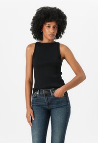Zwarte geribbelde tanktop met een hoge halslijn en mouwloos ontwerp, gecombineerd met donkerblauwe strakke jeans. De stof is zacht en gestructureerd.