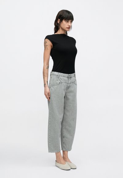 Haut noir à manches courtes côtelé associé à un jean large gris clair. La tenue est complétée par des chaussures plates beiges, offrant un look décontracté.