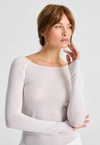 Világos rózsaszín, hosszú ujjú felső, puha anyagból, széles nyakkivágással, testhez simuló ujjal és kontrasztos varrással a vállaknál.