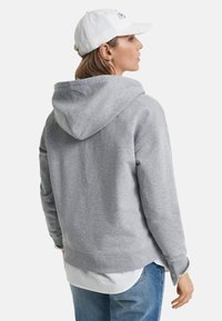 Hallhargune kapuutsiga sviiter, millel on lõtv lõige ja mis on valmistatud pehmest kangast. Omab känguru taskut ja soonikuga varrukaid. Kombineeritud valge särke all.