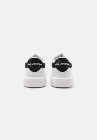 Paire de baskets blanches Karl Lagerfeld avec des languettes de talon texturées noires et des semelles blanches épaisses vues de dos sur un fond uni.