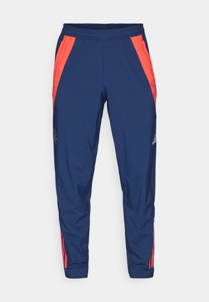 Pantaloni da jogging elasticizzati blu navy con strisce laterali arancioni, caratterizzati da un logo sulla gamba sinistra. Realizzati in tessuto liscio e leggero.
