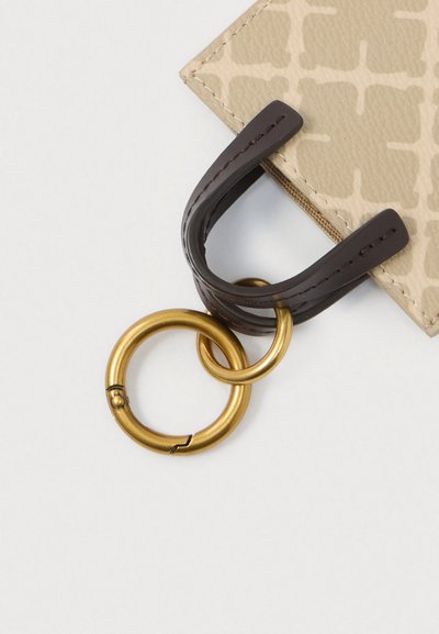 Beeži mustriga rahakott nurk koos kinnitatud tumeda nahkse aasaga ja kahe omavahel seotud kuldmetallist võtmerõngaga valgel taustal.