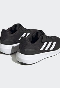 Zapatillas deportivas negras con parte superior de tela texturizada, diseño de tres franjas blancas y suela blanca en contraste con detalles de amortiguación.
