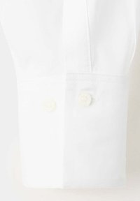 Poignet de chemise blanche à manches longues avec deux petits boutons blancs et coutures visibles sur fond clair uni.