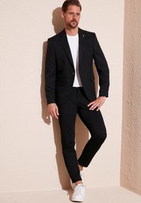 Must on musta ülikond, mille all on valge sooniline särk; see on kombineeritud mustade kitsaste pükstega ja valgete tossudega. Kanda on ka peen lips.