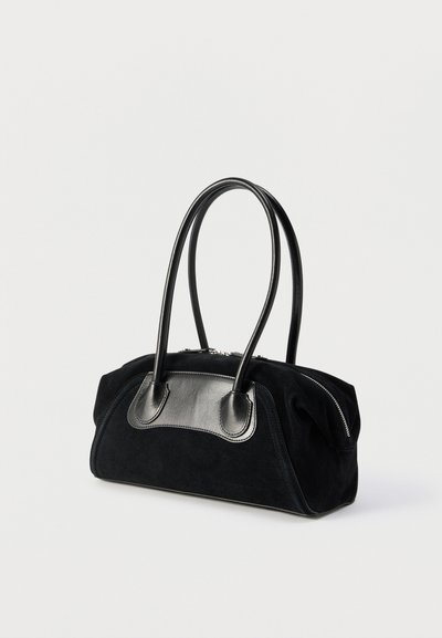 Τσάντα χειρός από μαύρο σουέντ με λαμπερά μαύρα δερμάτινα χερούλια και φερμουάρ, τοποθετημένη σε απλό λευκό φόντο.