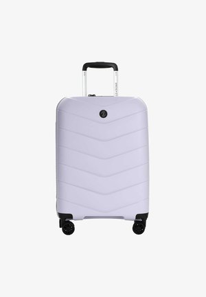Valise rigide violette avec poignée télescopique et quatre roues noires pivotantes, vue de face sur fond blanc.