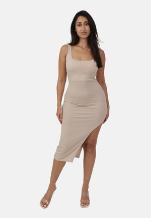 Beige geripptes Midikleid mit ärmellosem Design, quadratischem Ausschnitt und seitlichem Schlitz. Kombiniert mit transparenten Blockabsatz-Sandalen.