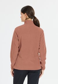 Fleecejacka i dammrosafärg, hög krage, långa ärmar, mjuk textur och platta sömmar. Enfaldig design utan synlig hårdvara eller mönster.