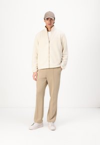 Cream fleece jacket with zip, beige trousers, and white sneakers. Simple design, soft texture, and light, neutral colors throughout.
