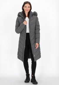 Grå, polstret lang frakke med en aftagelig hætte med pelsfor og kontrasterende zigzag-syninger. Har lynlås og sidelommer.