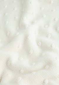 White knitted fabric featuring textured dotted patterns, soft and smooth texture, with a lightweight and cozy appearance.