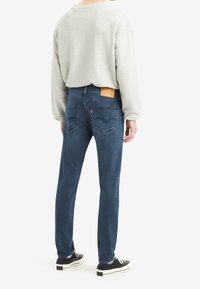 Light grey sweatshirt and dark blue jeans, featuring a leather back patch, straight leg design, and classic five-pocket style.