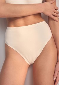 Slip bikini beige a vita alta con una texture liscia, caratterizzato da un'apertura curva per le gambe e un design minimalista senza motivi o accenti.