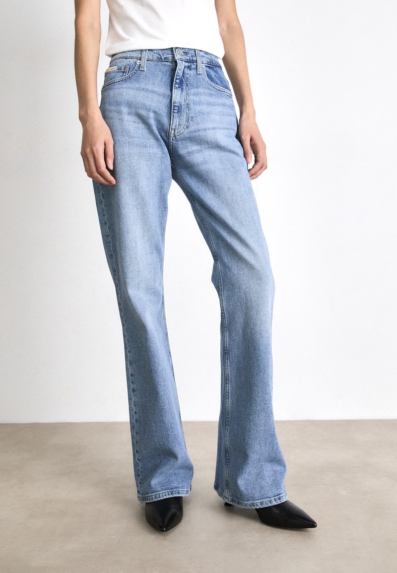 Vaqueros acampanados de denim azul claro con una cintura de altura media, un ligero desvanecimiento y detalles cosidos. Combinados con zapatos negros de punta afilada.