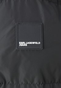 Svart boblejakke med teksturert stoff, firkantet logo-patch med hevede kanter, og hvit tekst som sier "KARL LAGERFELD JEANS."