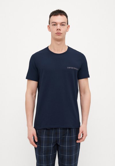 Tamsiai mėlynas medvilninis marškinėlis su apvaliu kaklu ir trumpomis rankovėmis, ant krūtinės puikuojasi nedidelis "Emporio Armani" logotipas.