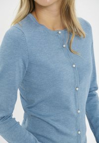 Šviesiai mėlynas kardiganas, pagamintas iš minkštos medžiagos, su apvalia iškirpte, ilgomis rankovėmis ir perlų formos mygtukais priekyje.