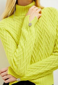 Knit sweater in fluorescent yellow with a textured herringbone pattern, featuring a high turtleneck and jeweled accents on the sleeves.