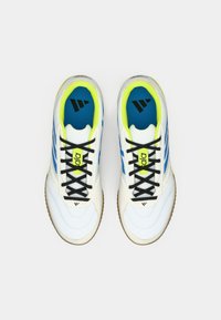 Bílé sportovní boty s modrými pruhy, černými tkaničkami a neonově žlutými akcenty. Mají texturovanou podrážku a polstrovanou modrou stélku s logem.