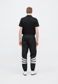 Černé polo tričko s klasickým límečkem, doplněné černými tepláky se stříbrnými vodorovnými pruhy na manžetách. Bílé tenisky.