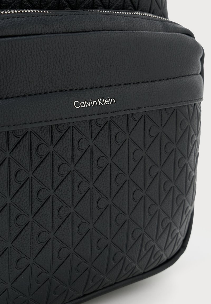 Black textured backpack featuring a geometric pattern, smooth accents, and a metallic Calvin Klein logo on the front.