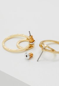 Goldene Creolen mit strukturierter Oberfläche und einem kleineren, kontrastierenden Gold- und Silberstiftverschluss für sicheren Halt.