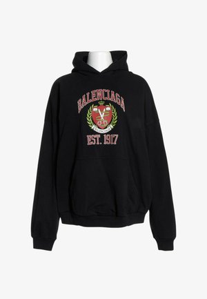 Sweat à capuche noir avec poche avant, motif de blason rouge et vert, texte "BALENCIAGA" au-dessus et "EST. 1917" en dessous sur la poitrine.
