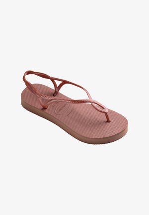 Lyserød flip-flop med en struktureret fodbund, tynde remme med flettede detaljer og en lavprofil gummisål.