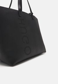 Borsa tote nera con manici sottili, caratterizzata dal nome del marchio "ORCIH" perforato verticalmente sul lato su sfondo bianco.