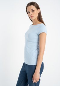 Jasnoniebieska koszulka z krótkim rękawem i okrągłym dekoltem. Wykonana z gładkiego materiału, o dopasowanym kroju i subtelnych detalach przeszyć na rękawach.