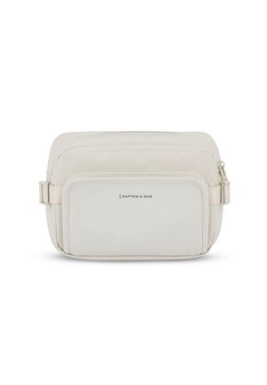Personne portant un jean noir à jambes larges, un haut gris à manches longues, des baskets blanches et un sac bandoulière beige sur un fond blanc uni.