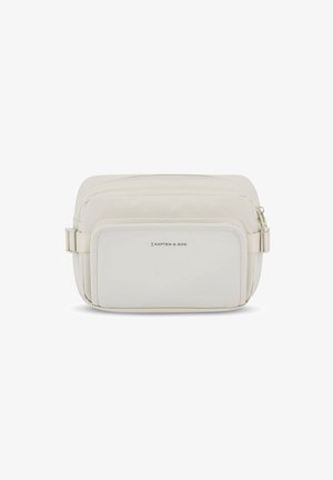 Personne portant un jean noir à jambes larges, un haut gris à manches longues, des baskets blanches et un sac bandoulière beige sur un fond blanc uni.