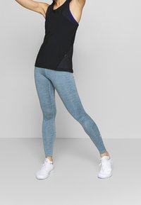 Czarny sportowy top na ramiączkach z niebieskimi akcentami, w połączeniu z jasnoniebieskimi, dopasowanymi legginsami. Białe sneakersy dopełniają stylizację. Gładki, elastyczny materiał.