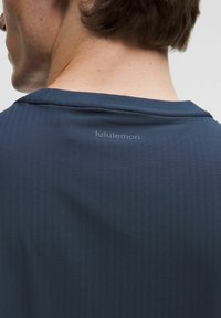 Námorná športová tričko s okrúhlym výstrihom, ryhovanou textúrou a značkovým logom na zadnej strane. Tkanina sa zdá byť ľahká a priedušná.