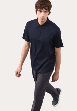 Polo bleu marine à manches courtes avec une patte de boutonnage, associé à un pantalon fuselé gris foncé et des baskets noires à semelle blanche.