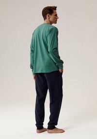 Zielona koszula z długim rękawem, wykonana z miękkiego materiału, w połączeniu z granatowymi spodniami. Charakteryzuje się luźnym krojem, okrągłym dekoltem i prostym designem.