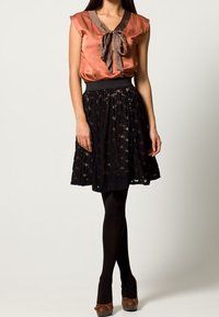 Satinblus i rost med brunt band, kombinerad med en svart spetkjol. Modellen bär svarta strumpbyxor och bruna klackar; outfiten har en figursydd midja.