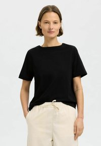 Svart bomulls t-shirt med rund halsringning och korta ärmar, kombinerad med beige byxor med dragsko. Enkelt mönster, mjuk textur.