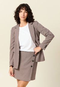 Ruudullinen bleiseri ruskeassa ja kermanvärisessä sävyssä, jossa on kaksinkertaiset napit, yhdistettynä yhteensopivaan polvipituiseen hameeseen, jossa on sivunapit.