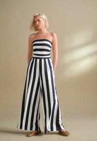 Strapless jumpsuit i marinblått och vitt med vertikala ränder, med en åtsittande livdel och vida byxor. Slät tyg, lätt design.