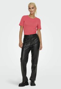 Suéter rosa de manga corta combinado con pantalones de imitación cuero negros que cuentan con bolsillos frontales, un corte relajado y zapatos negros de suela gruesa.